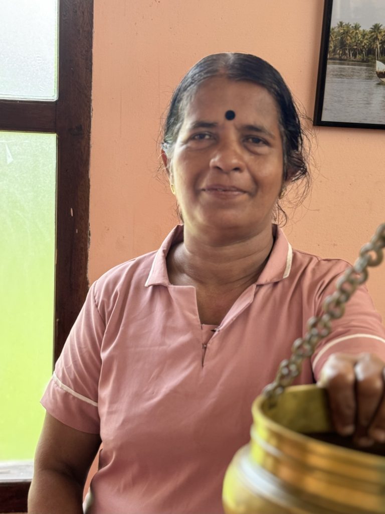 Sulekha -Massage Therapist at Prakruthi Ayurveda, Cherai Beach, holds a brass vessel for Shirodhara