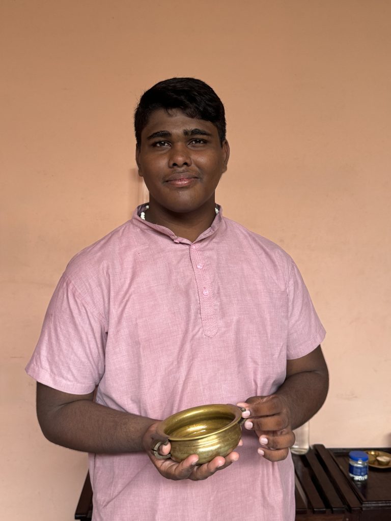 Linto - massage therapist at Prakruthi Ayurveda, Cherai Beach, holds a brass vessel